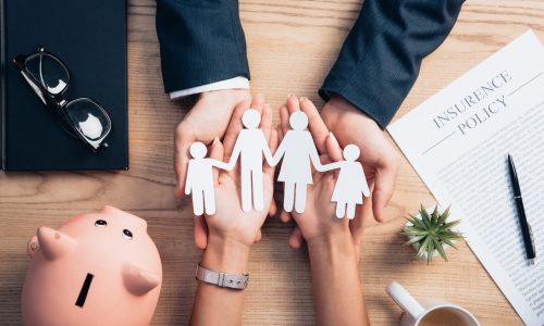 top view of lawyer and woman holding paper cut family near cup of coffee, insurance policy